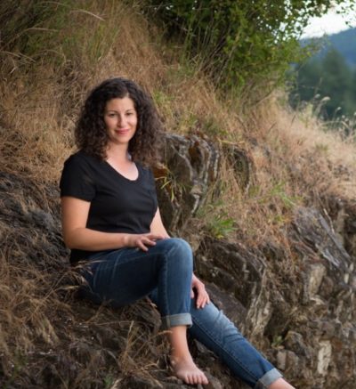 Claire is sitting on ground outdoors smiling.