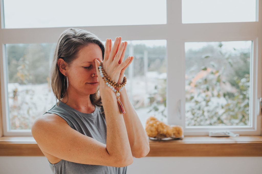 Tash with mala beads wrapped around her hands in prayer at forehead.