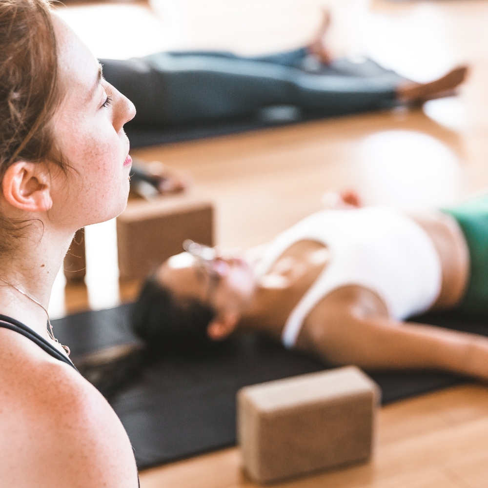 A teacher watches a class in savasana (corpse pose)